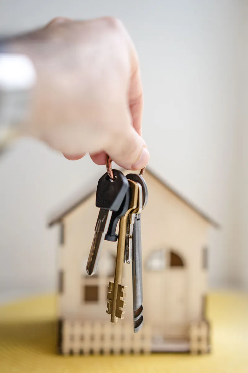 Hand met huissleutels boven een huismodel